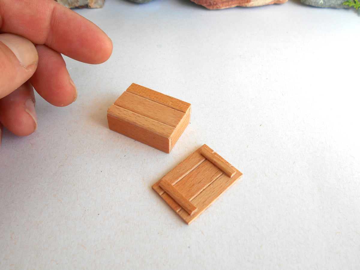 Two miniature wooden door or panel pieces displayed on a white surface, with a person's fingers visible at the left edge for scale.