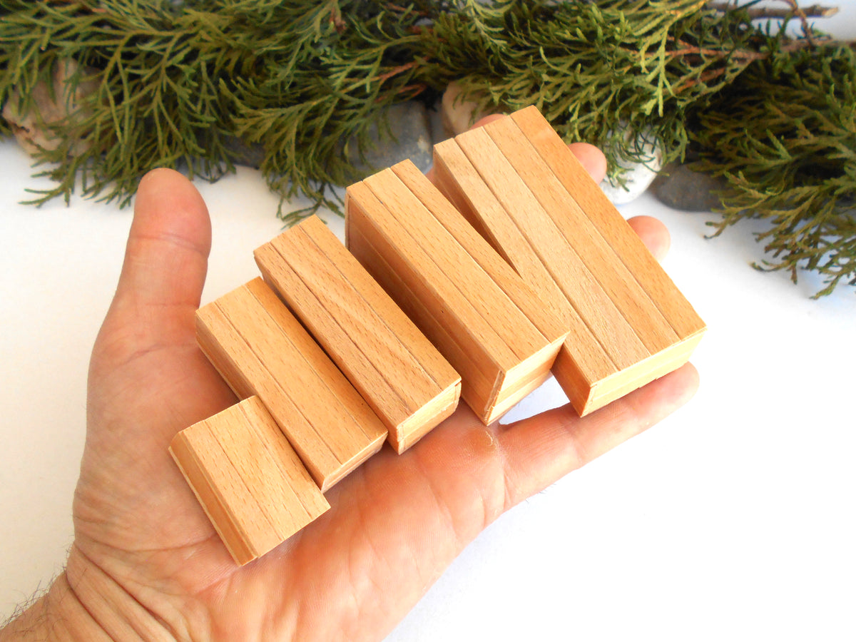 Four small rectangular wooden miniature boxes in different sizes held in a person's hand, with green foliage and gray stones in the background.