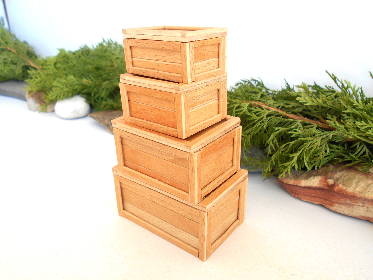 Four small stacked wooden crates in a warm natural wood finish, set against a white background with green foliage props.