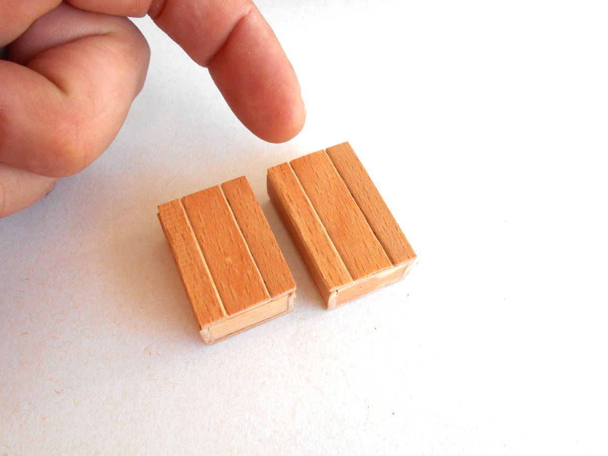 Two miniature wooden miniature box with a slatted design, shown next to a person's finger to indicate their small scale, on a plain white background.