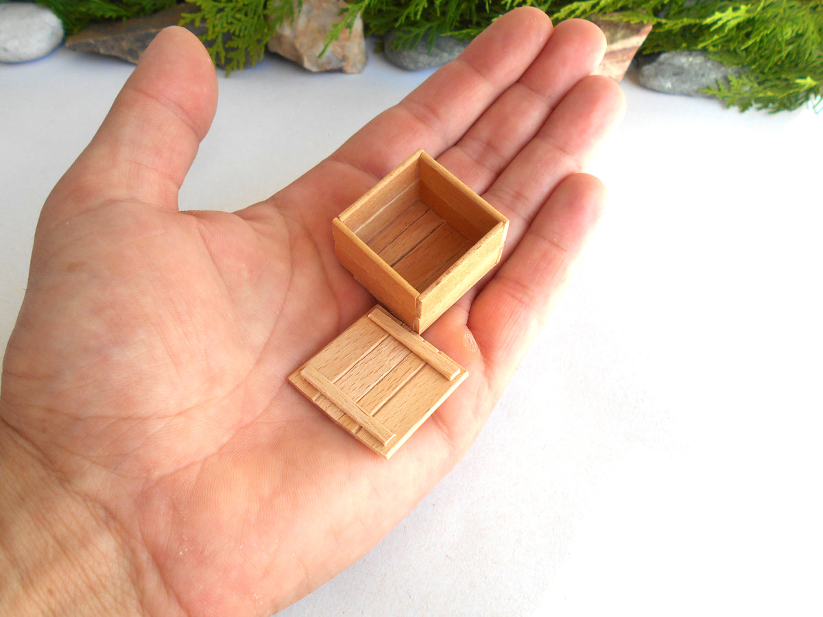 A miniature light brown wooden box with its lid placed beside it, held in the palm of a hand to show its small scale.