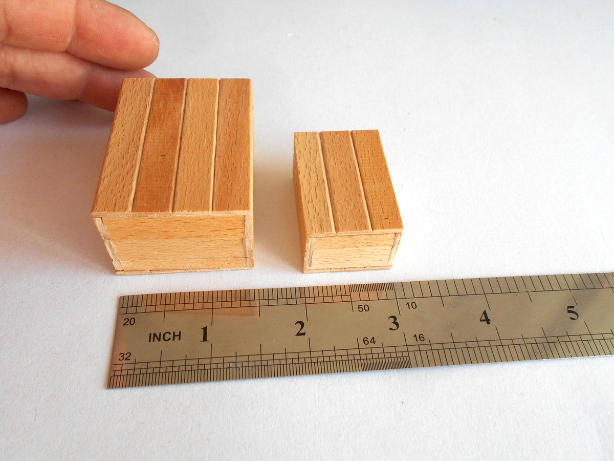 Two small wooden blocks with a slatted design, shown next to a metal ruler for scale and held by a hand on a white background.