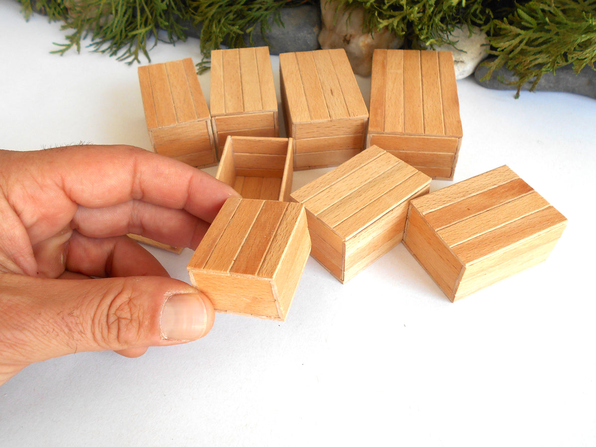 A hand holding a small rectangular wooden box, with several matching miniature wooden boxes arranged on a white surface in the background.