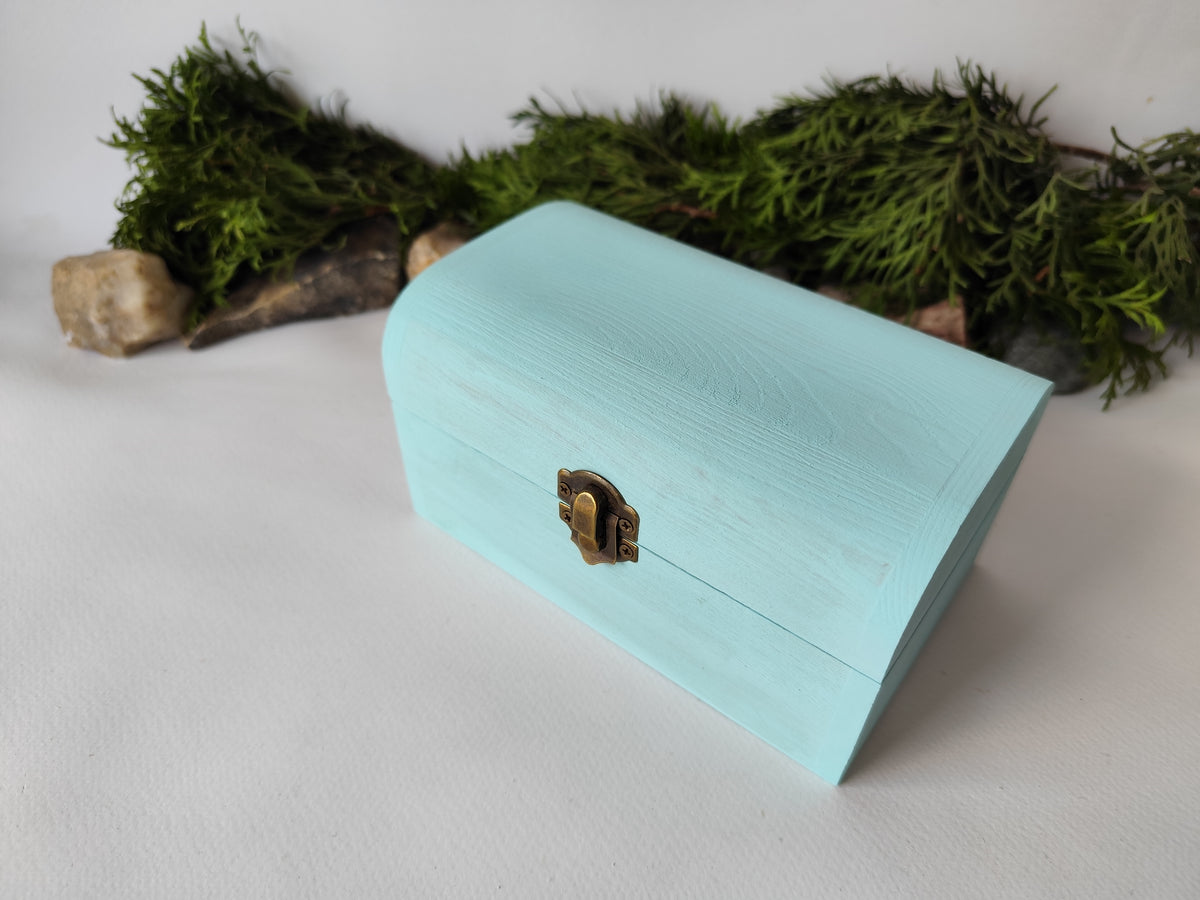 This mint painted chest wooden box is made of quality pine wood and has metal hinges with bronze-color and the cap and the body of the box have bronze-color closing. The cap of the small box is curved like in a chest box. The thickness of the box walls is 0.3 inches which makes the box strong and lasting. I have refined and sanded the box to have smooth surface and I have colored it with a mint light blue color that I developed myself with white, blue,  and green acrylic paints.