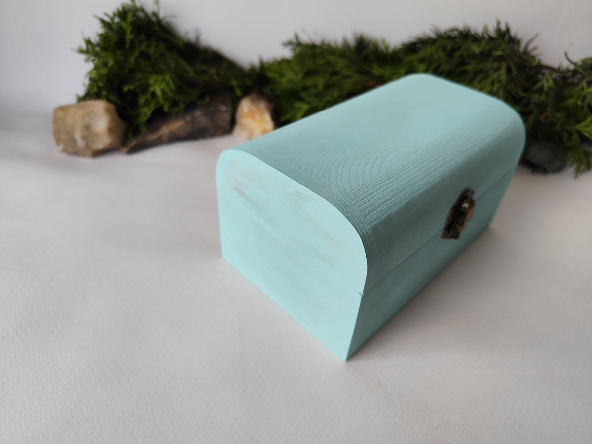 This mint painted chest wooden box is made of quality pine wood and has metal hinges with bronze-color and the cap and the body of the box have bronze-color closing. The cap of the small box is curved like in a chest box. The thickness of the box walls is 0.3 inches which makes the box strong and lasting. I have refined and sanded the box to have smooth surface and I have colored it with a mint light blue color that I developed myself with white, blue,  and green acrylic paints.